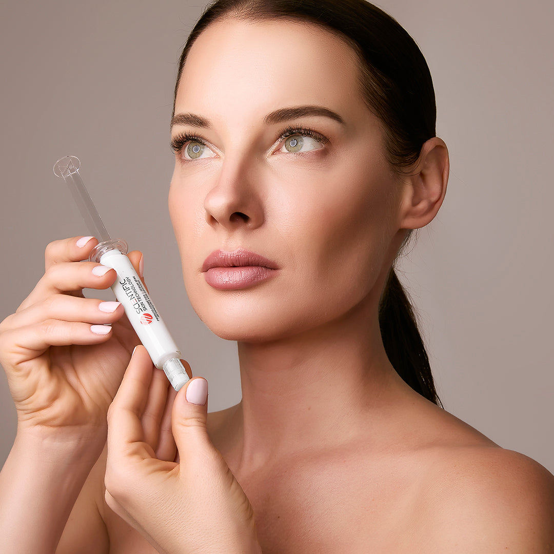 A person holds a skincare syringe-like product, looking upward.